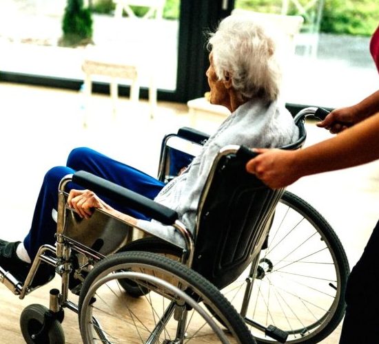 Medicinska sestra gura stariju osobu u invalidskim kolicima u domu za starije
