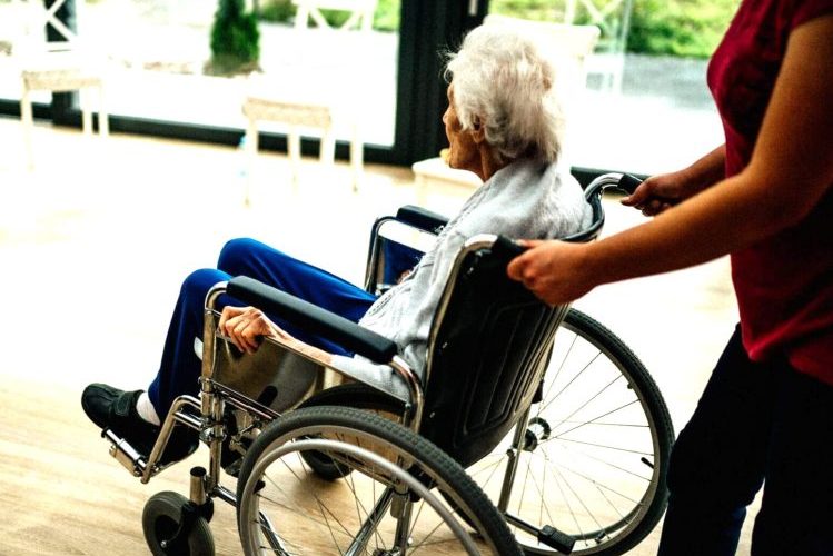 Medicinska sestra gura stariju osobu u invalidskim kolicima u domu za starije