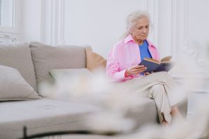 Starija žena sjedi sama kod kuće i čita knjigu